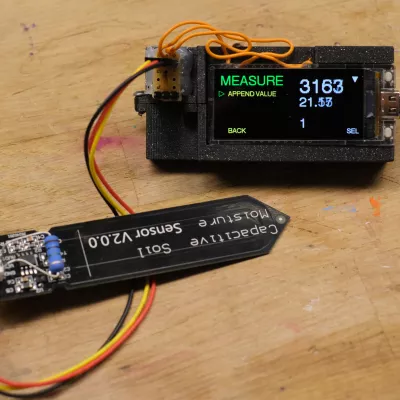 Ein Mikrocontroller mit Display in ein Gehäuse eingebettet. Daran angeschlossen ein kapatitiver Bodenfeuchtigskeitssensor